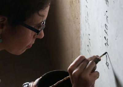 Con un pincel de caña y tinta negra hecha a base de humo, Lucía escribe sobre la pared enlucida.