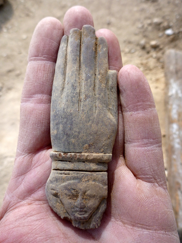 Extremo de un crótalo de madera con cabecita de Hathor tallada en la muñeca de un brazo.