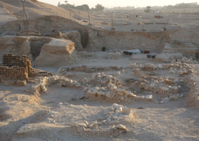 Capilla de ofrendas con el recinto delimitado por un murete de adobe delante. Las piedras son del saqueo de su pozo funerario.